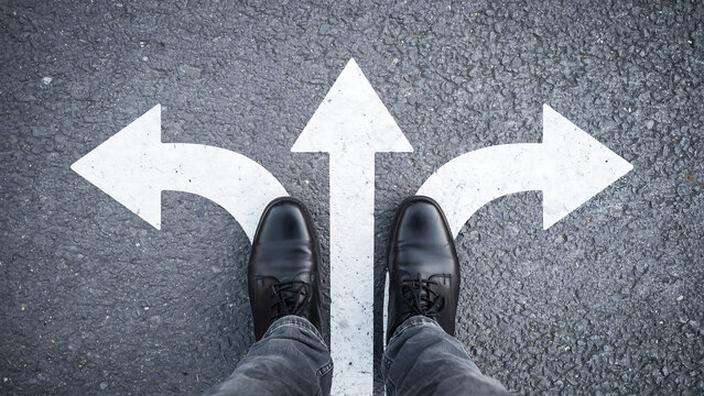 Person wearing formal shoes standing at a three-way intersection path on asphalt with crossroads decision direction business strategy lifestyle planning motivation conceptual