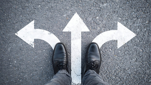 Individual facing three different paths painted on ground representing making a difficult life choice with decision crossroads direction strategy opportunity pointing navigation thinking