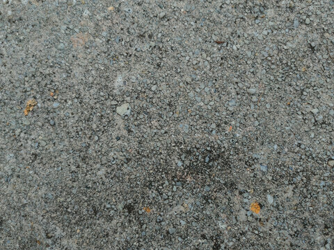A flat top-down view of an exposed aggregate concrete surface with fine pebbles, stones, and gray cement texture