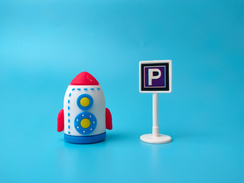 A toy rocket positioned next to a miniature parking sign with the letter P over a solid blue background