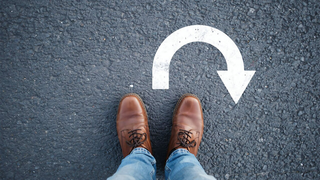 Person wearing brown shoes looking at u-turn sign painted on ground with u turn decision direction lifestyle navigation opportunity challenge motivation