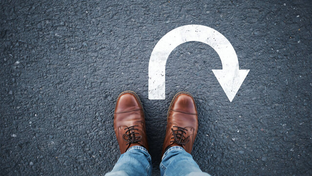 Conceptual image of person standing before u-turn white painted marking on pavement with u turn decision direction lifestyle navigation opportunity challenge motivation
