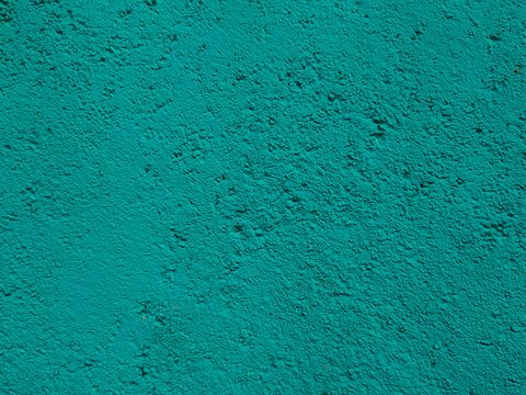 A uniform, textured wall surface coated in bright teal stucco paint showing fine grain and bumpy stipple patterns