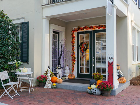 A residential front entrance is decorated with pumpkins, flowers, skeletons, lights, and seasonal Halloween ornaments. The festive autumn display creates a welcoming holiday atmosphere outside the