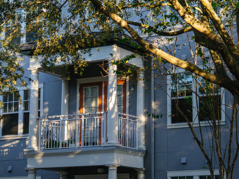 A contemporary apartment building features a balcony framed by leafy trees and warm sunlight. The elegant residential architecture creates a peaceful urban living environment.