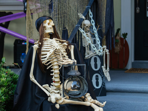 Halloween skeleton decorations with lanterns and spooky props decorate the front porch of a home. Seasonal ornaments create a festive and eerie Halloween holiday display.