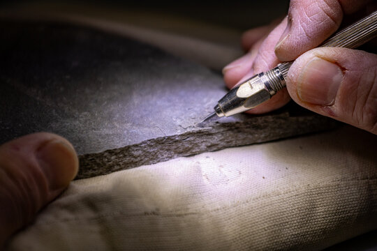 Gaspesie, Canada, 16 June 2026 : A person's hand uses a specialized tool to meticulously work on a delicate layered rock specimen.