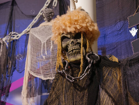 A frightening Halloween skull decoration with chains and tattered fabric hangs among haunted house decorations. Cobwebs and eerie props create a spooky Halloween display.