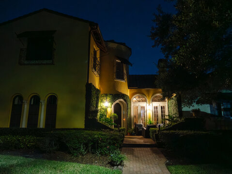 An elegant Mediterranean style residence glows with warm exterior lighting under a clear night sky. Landscaped gardens and arched architecture create a welcoming luxury home exterior.