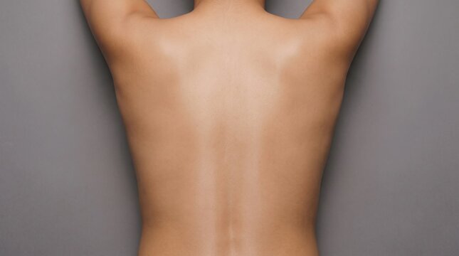 Back view of smooth clean female back and shoulders against grey background