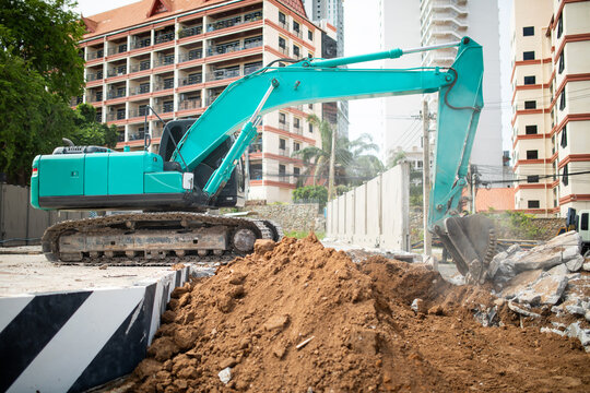 Green tracked excavator digging soil near pile of earth at urban construction site