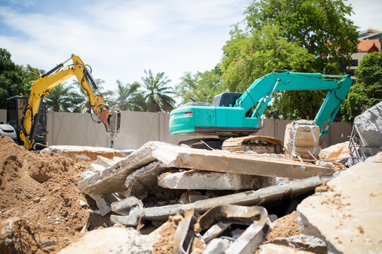 Broken Concrete Slabs And Dirt At Construction Demolition Site With Yellow Hydraulic Breaker And Green Excavator Working In Background