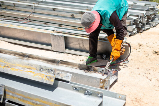 Construction Worker In Protective Gloves Cutting Steel I-Beam With Oxy-Fuel Gas Cutting Torch Outdoors At Building Site