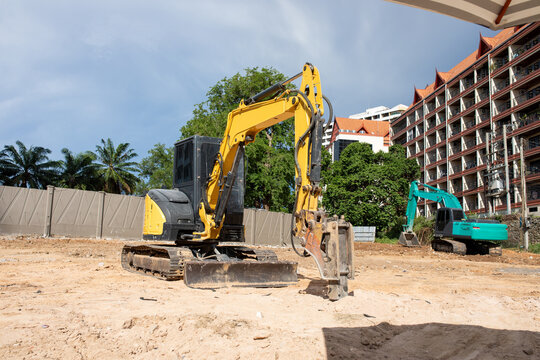 Yellow Excavator With Hydraulic Breaker And Green Digger Parked On Sandy Ground At Urban Construction Demolition Site