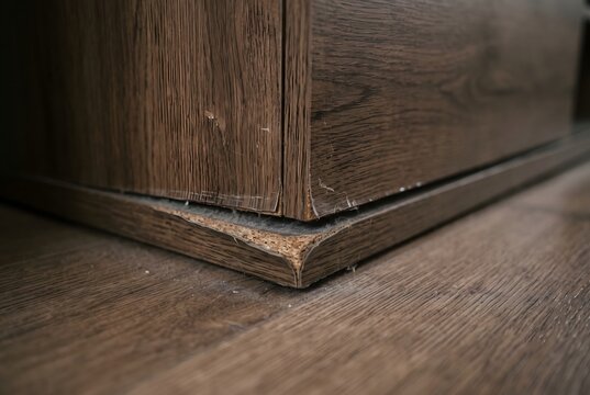 Macro close up of the bottom corner of a TV stand showing a peeling edge and fine dust