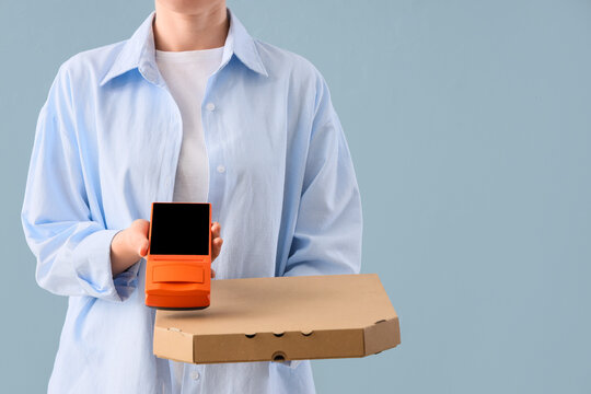 Person in blue shirt holding a pizza box and an orange payment terminal for contactless delivery service, Modern contactless delivery services and secure payment transactions