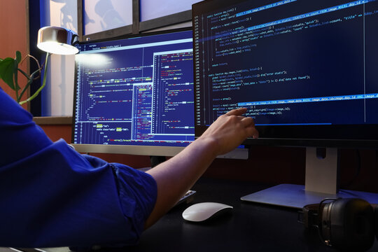 Programmer working on multiple computer screens displaying code, software development and data analysis
