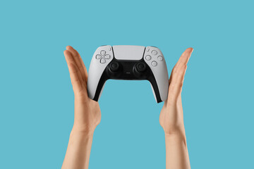 Hands holding a modern white video game controller with black accents, gaming and entertainment concept on a blue background © Pixel-Shot