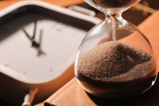 Hourglass with sand flowing and a blurred clock in the background, time passing and deadlines