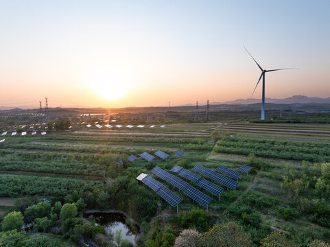 Wind turbine and solar panels on farmland during sunset with rolling hills and green vegetation
