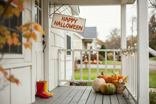 Happy Halloween sign hanging on a cozy front porch, autumn house entrance with pumpkins and string lights, seasonal fall home exterior decor