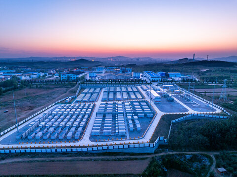 Large-scale energy storage power station at sunset with orderly battery arrays and industrial facilities