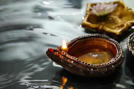 Diya lamps with beautiful flower in water on green background. Divaly celebration
