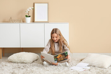 Fototapeta premium Little girl reading book while sitting on floor at home