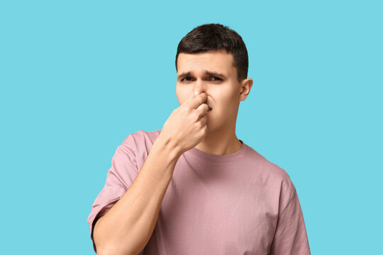 Handsome young man pinching nose because of bad smell on blue background