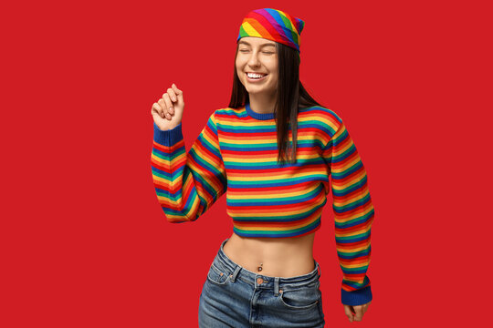 Beautiful young happy woman in rainbow sweater with piercing navel on red background