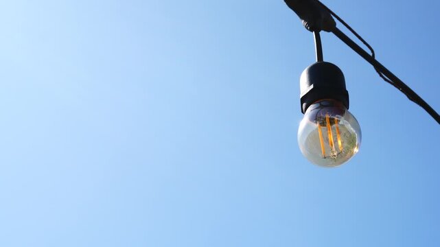 Vintage filament light bulb hanging outdoors against blue sky