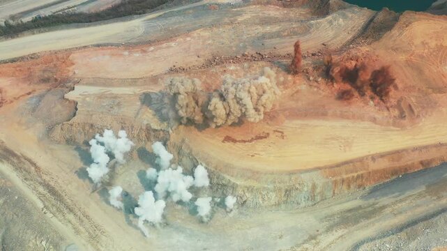 Rock blasting in an open pit mine for production and rehandle operations, illustrating controlled drilling and blasting used to fragment rock for efficient excavation, loading, and material handling i