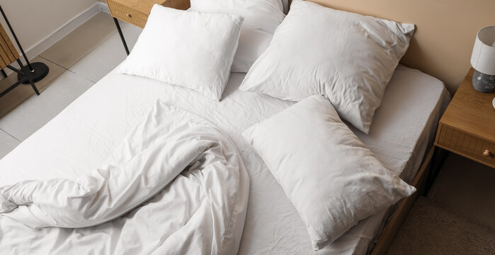 Unmade bed with white sheets and pillows in a modern bedroom, comfort and relaxation concept, morning routine