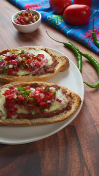 Mexican molletes with cheese and refried beans with a white bowl with pico de gallo