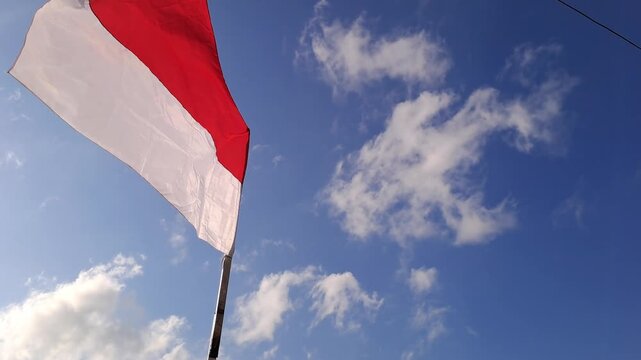 Low angle view of Indonesian flag waving in left side against blue sky with clouds. Red and white national flag. Patriotic and independence day symbol.