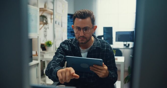 Young Caucasian male developer uses digital tablet to inspect software coding algorithms at office desk. Programming development, Artificial intelligence machine learning, Secure database concept.