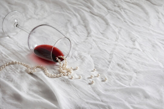 infidelity. Overturned red wine glass and scattered pearls on crumpled white tablecloth, scandal and infidelity concept, bar promotions.