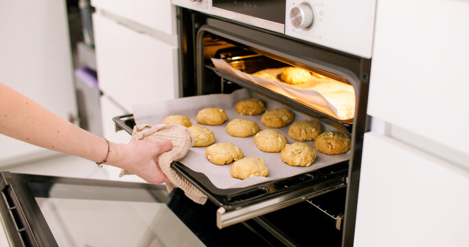 Baking cookies. Pastry preparation. Woman confectioner hand taking hot metal tray with sweet peanut round treat from modern home oven.