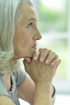 elderly woman holding hands with another person in a comforting indoor setting, possibly a home or care environment, close-up focusing on hands and face, gray and white tones.