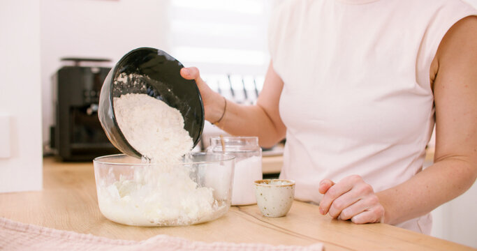 Preparing dough. Adding flour. Woman chef hand pouring white culinary ingredient in glass bowl cooking tasty pastry at home kitchen.