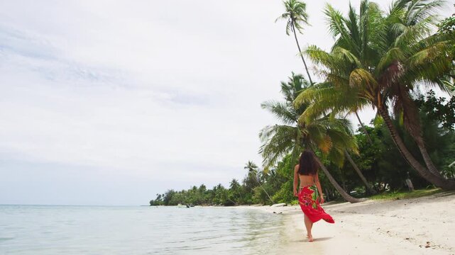 Vacation travel woman relaxing on paradise beach with palm trees on holidays. Girl on beach in pareo and bikini on Tahiti, French Polynesia. Vertical video of real woman model without any makeup