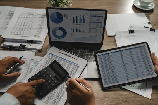 Business people meeting financial documents with calculator, and laptop charts on a desk, comparing figures and discussing data analysis for reporting and budgeting.