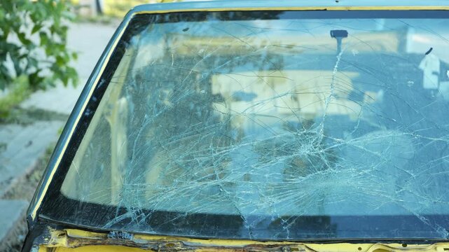 Broken windshield on old yellow car showing extensive damage and shattered glass