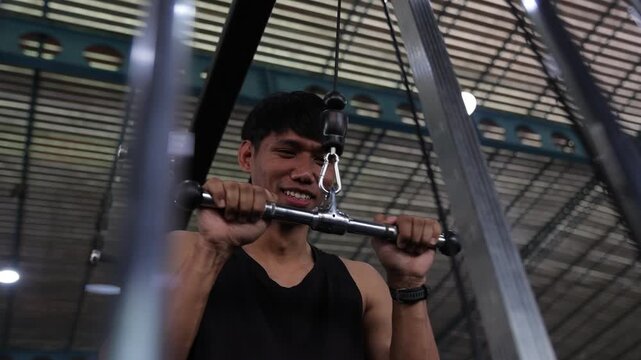Young athletic Asian man concentrating while performing a triceps pushdown exercise on a cable machine. A fitness lifestyle routine.