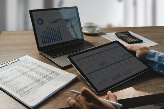 Tablet and laptop display financial dashboards beside printed reports and a calculator, showing data analysis and planning workflow for accounting review and business report evaluation.