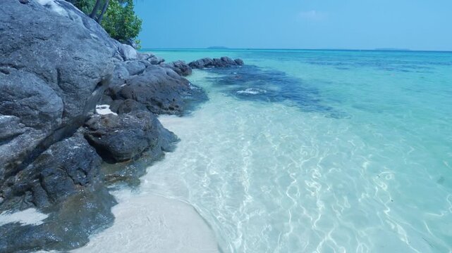 Slow motion: waves on rocky tropical shoreline with crystal clear turquoise sea in Karimunjawa National Park Indonesia lush vegetation and tranquil island scenery