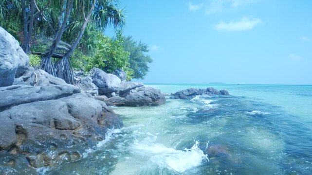 Slow motion: waves on rocky tropical shoreline with crystal clear turquoise sea in Karimunjawa National Park Indonesia lush vegetation and tranquil island scenery