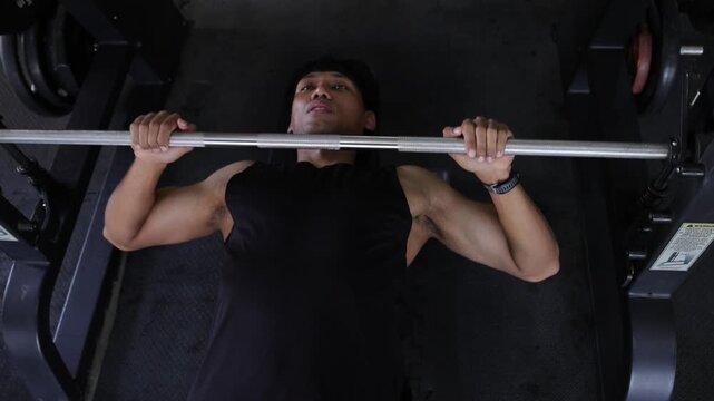 Strong man lifting heavy barbell on bench press. Athletic man performing chest press exercise using a barbell on a smith machine. Upper body strength training at the gym for fitness.