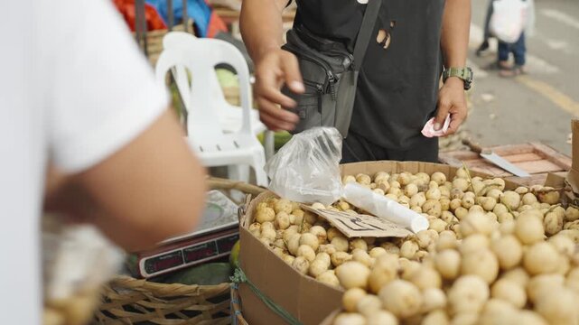 Vendor Handing Packaged Langsat Fruit to Customer at Local Market