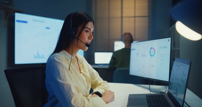 Team young Asian businesswoman working late talk on telephone headset in call center office at night. Corporate customer service support, telemarketing, finance insurance investment advisor concept.